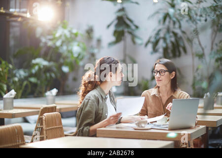Portrait of two young businesswomen discussing project sitting at table in designer cafe, copy space Stock Photo