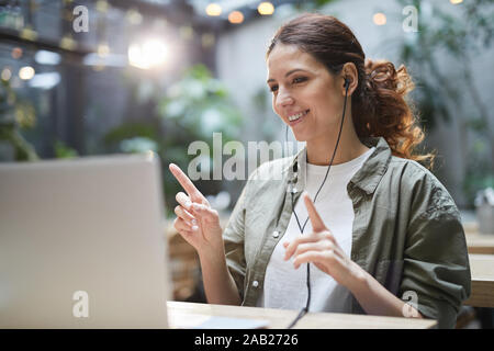 Portrait of modern young woman listening to music and dancing while using laptop on outdoor terrace in cafe, copy space