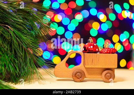 a close-up of a wooden truck brought red Christmas balls to a Christmas tree on the background of many colorful lights. Picture for New Year's design, Stock Photo