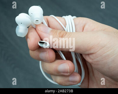 Close-up of hand holding a pair of white USB-C earphones against a dark background Stock Photo