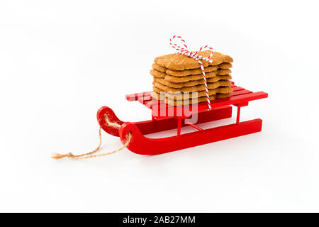 Spekulatius, Speculaas, Speculoos, spiced Christmas cookies on red wooden sledge isolated on white. Angled view. Stock Photo