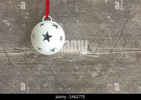 Closeup of a white hanging jingle bell on dark brown, rustic weathered wood with copy space. Top view. Stock Photo