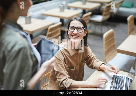 High angle portrait of young woman looking at waitress and smiling while working in cafe , copy space Stock Photo