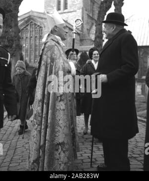 1964, historical, a high-ranking Roman Catholic priest wearing an embroidered dalmatic or gown, biretta (hat) and holding a crosier or staff talking to an elderly gentleman wearing a bowler hat outside St Mary's church, Aylesbury, England, UK. Stock Photo