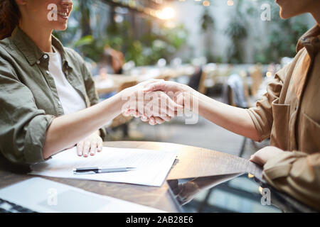 Side view close up of two young women shaking hands across table during business meeting in cafe, copy space