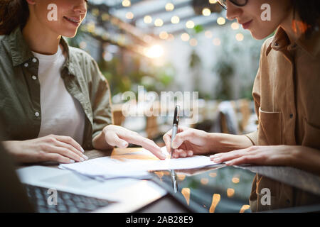 Close up of two young women signing contract during business meeting in cafe, copy space Stock Photo