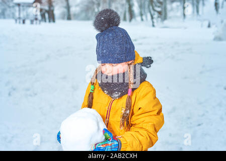 little girl sculpts a snowman in winter