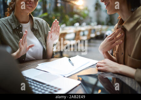 Close up of unrecognizable young woman gesturing actively during business meeting in cafe with female partner across table, copy space Stock Photo