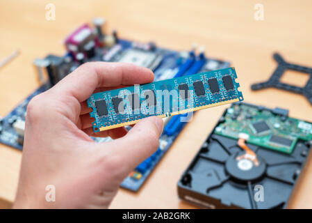 RAM memory module in hand. Motherboard and hard disk in background. Concept of installation. Stock Photo