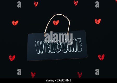 Welcome wording on black notice board  with red hearts around Stock Photo