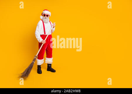 Full body photo of serious brutal worker hipster santa claus in red hat wipe broom on x-mas time noel celebration wear black boots isolated over Stock Photo