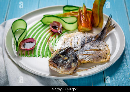 Fried fish dorado, decorated with cucumbers and onions. On a blue wooden background Stock Photo