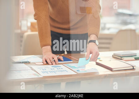 Cropped portrait of young businessman sorting documents and data while planning project behind glass wall in office, copy space Stock Photo
