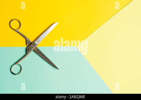 Flat lay of opened scissors over turquoise blue and yellow background. conceptual photo of cutting scissors with central composition Stock Photo