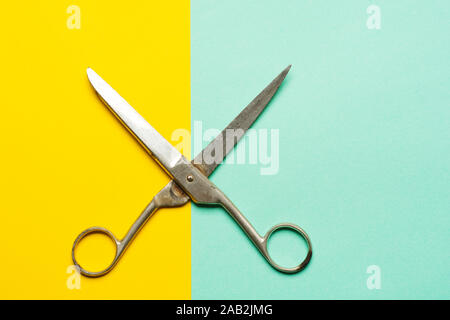 Flat lay of opened scissors over turquoise blue and yellow background. conceptual photo of cutting scissors with central composition Stock Photo