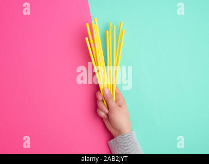 hand holds a stack of yellow paper tubes for a cocktail on a multi-colored background, concept of rejection of plastic and the use of recyclable mater Stock Photo