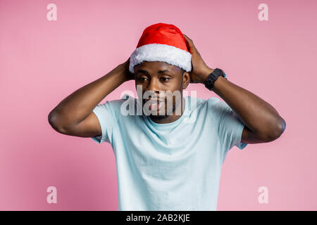 Surprised african american man with beard, wearing Santa hat, looking aside with amazed expression, remembered something important, touching head with Stock Photo