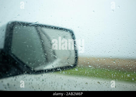 Driving on a highway a rainy spring day. Raindrops on the car window and on the wing mirror, cloudy sky, blur countryside Stock Photo