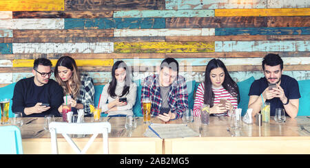 Group of young friends using mobile smart phone at pub restaurant table for social media Stock Photo