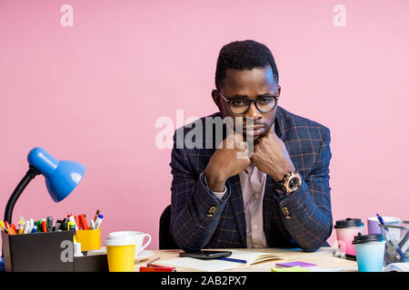 Portrait of tired unhappy young dark skinned manager sitting at workplace, having financial problem, thinking, looking off into distance. People, busi Stock Photo