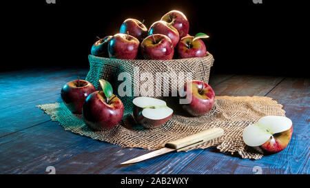 Fresh whole and half cut apples in a bowl on wooded table with knife . Stock Photo