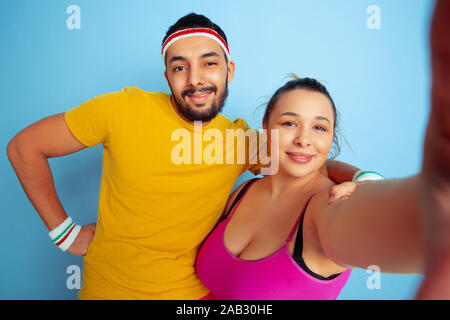 Young pretty caucasian couple in bright clothes training on blue background Concept of sport, human emotions, expression, healthy lifestyle, relation, family. Making selfie together and hugging. Stock Photo