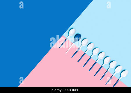 Concept of white plastic spoons on tricolor blue pink background. Flat lay, top view, copy space. Stock Photo