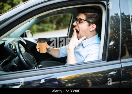 Young man feeling tired and yawning while driving a car Stock Photo