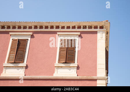 Close up of the exterior of a old pink colored house with white details and wooden louvre windows half closed. Typical mediterranean style. On a sunny Stock Photo