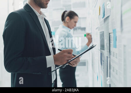 Corporate business team analyzing financial reports hanging on a wall and planning business strategies Stock Photo