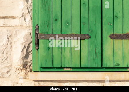 Close up of the exterior of  green painted closed wooden barn window blinds with metal details and the light colored limestone wall with big stone pie Stock Photo