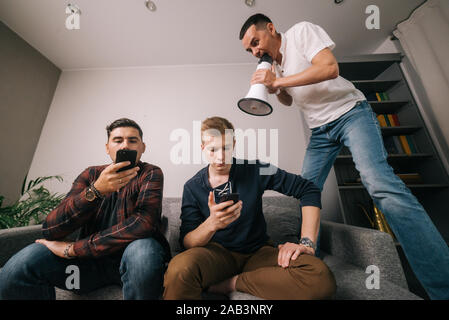Young man shouting through a loudspeaker at friends which using a mobile phone Stock Photo