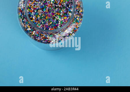 Crushed plastic pellets, parts made of multicolored recycled plastics collected at sea in a glass jar, blue background ready to be used for new circul Stock Photo