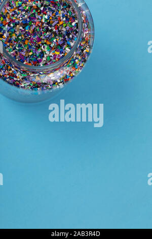 Crushed plastic pellets, parts, particles made of multicolored recycled plastics collected at sea in a glass jar, blue background ready to be used for Stock Photo