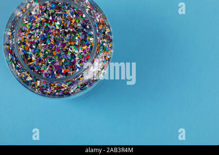 Crushed plastic pellets particles made of multicolored recylced plastics collected at sea in a glass jar on a blue background ready to be used for new Stock Photo