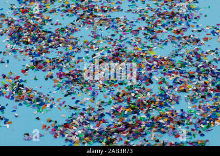 Circular crushed plastic pellets, parts made of multicolored recycled plastics collected at sea flatlay spread on a blue background to be used for new Stock Photo