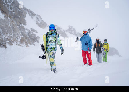 Photo of four sports people with skis and snowboard walking in winter resort in afternoon Stock Photo