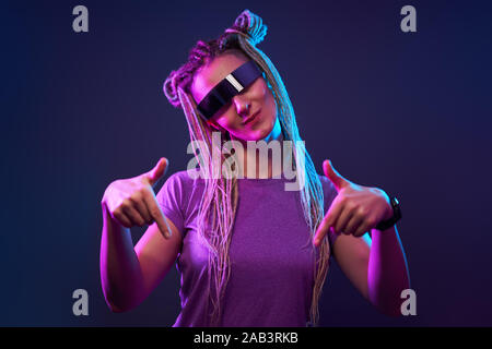 Happy girl with pigtails in sunglasses looking at camera in neon light at disco Stock Photo