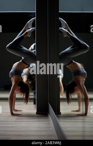 Sportwoman stands on her hands against gray wall in gym Stock Photo