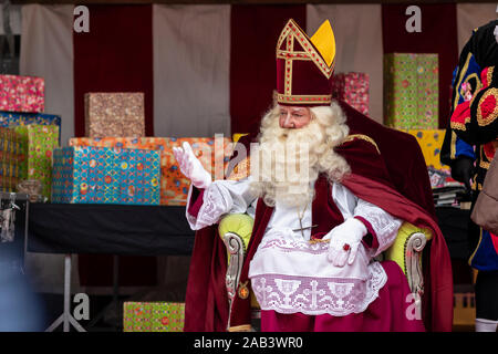 Eindhoven, The Netherlands, November 23rd 2019. Sinterklaas wearing his costume sitting on a chair waving to childeren. Wrapped colorful gifts in the Stock Photo