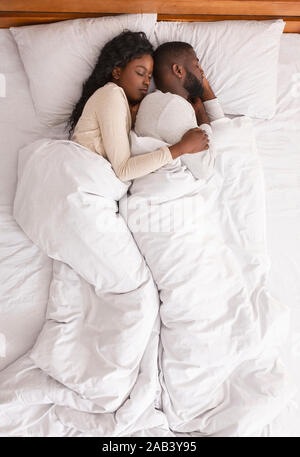 Afro couple hugging while sleeping together in bed, top view Stock Photo