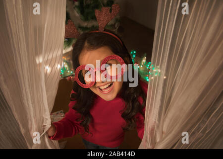 Portrait of a happy young girl wearing antlers and an eye mask prop during Christmas. (Children) Stock Photo