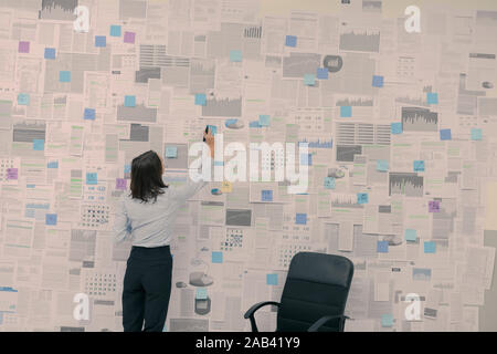 Corporate businesswoman checking financial data and reports hanging on a wall, management and strategy concept Stock Photo