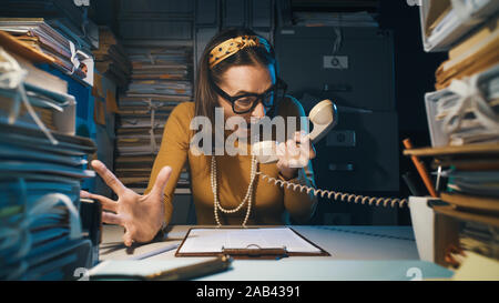 Stressed angry secretary shouting at customers on the phone, she is overloaded with work Stock Photo