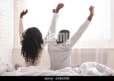 Relaxed afro couple sitting on bed, stretching after sleep Stock Photo