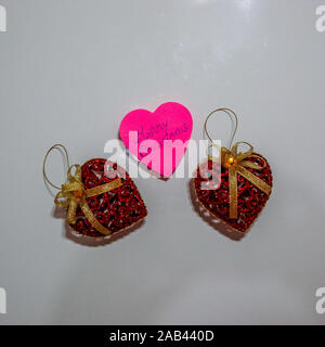Christmas decorations on white board. Christmas concept, glittery heart shaped Christmas balls and pink post it with Merry Christmas. Stock Photo