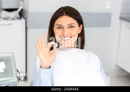 Satisfied pretty parient in dentist chair showing okay Stock Photo