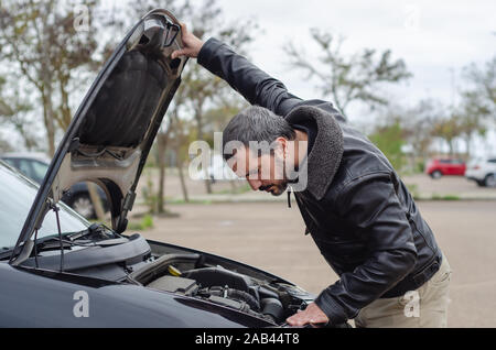 worried mature man looking under the hood of breakdown car Stock Photo
