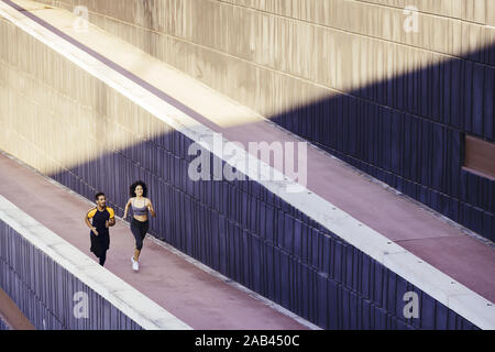 happy young woman and sports man running on the city street in modern environment of walls. fitness, urban sports workout and healthy lifestyle concep Stock Photo