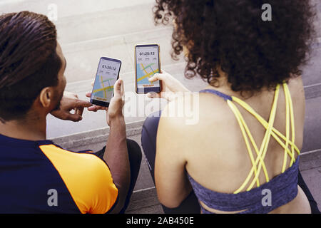 rear view of a interracial athletic young couple looking the sports app in their mobile phones on the stairs during a rest in the workout, technology Stock Photo